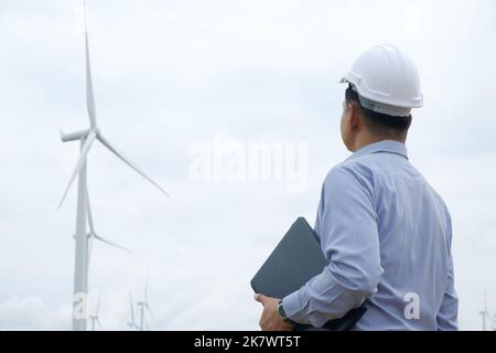 Ingenieure arbeiten an Windmühlen mit Laptop und der Windturbine im Hintergrund. Konzept der Nachhaltigkeitsentwicklung durch alternative Energien Stockfoto