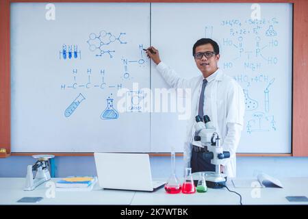 Wissenschaftslehrer schreibt im Klassenzimmer an der Tafel Stockfoto
