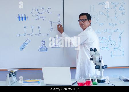 Wissenschaftslehrer schreibt im Klassenzimmer an der Tafel Stockfoto