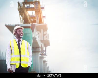 Afrikanischer Tiefbau arbeitet mit Tablet zur Steuerung des Straßenumbaus und inspizieren die Baustelle mit Walzenverdichter-Maschine auf einem Stockfoto