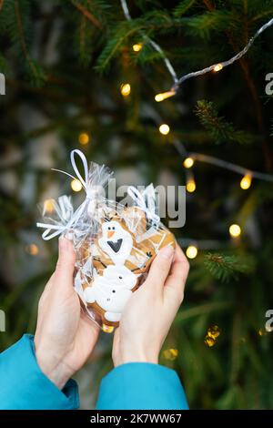 Eine Frau hält Lebkuchen in Form eines Cartoon-Schneemanns in ihren Händen auf dem Hintergrund eines grünen Weihnachtsbaums im Freien. Das Konzept des Winters Stockfoto