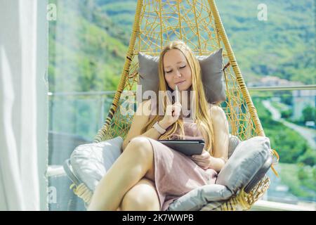 Kaukasische Frau, die auf der Terrasse sitzt und von zu Hause aus mit einem Computer-Laptop arbeitet. Junge Frau unterrichtet eine Fremdsprache oder lernt eine Fremdsprache Stockfoto