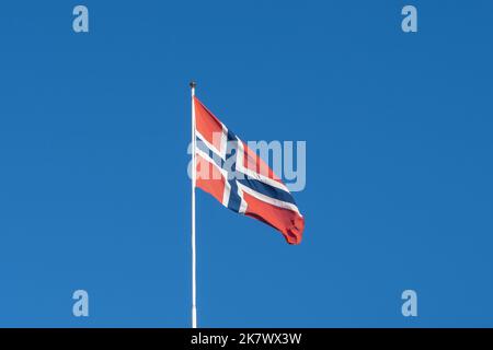 Eine winkende Flagge Norwegens mit blauem Himmel im Hintergrund. Stockfoto