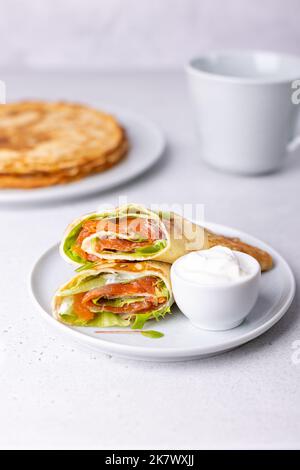 Pfannkuchen mit Lachs (Forelle), Sauerrahm und Grünzeug. Dünne, nicht süße Blinchiki, gefüllt mit rotem Fisch. Traditionelles russisches und ukrainisches Gericht. Stockfoto