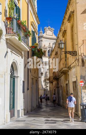 Junger Mann, der entlang der Via Del Palazzo dei Conti di Lecce in Richtung der Matthäuskirche im historischen Lecce, Apulien (Apulien), Italien, geht. Stockfoto