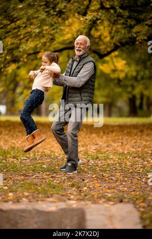 Der gutaussehende Großvater verbringt am Herbsttag Zeit mit seiner Enkelin im Park Stockfoto