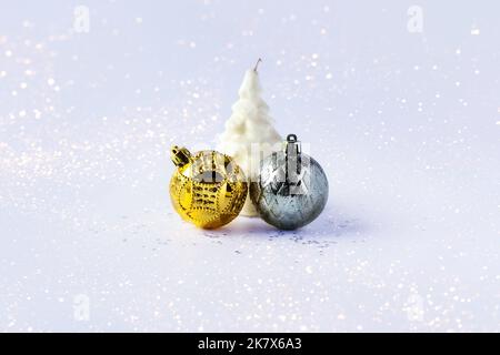 Weihnachtskomposition aus goldenen und silbernen Weihnachtskugeln und einer weißen Weihnachtsbaumkerze auf grauem Hintergrund mit Sternen Stockfoto