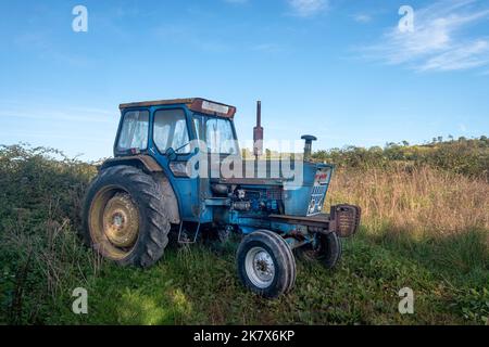 Alter, rostiger blauer Traktor, der auf einem Feld sitzt Stockfoto