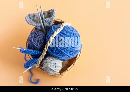 Blaue Strickgarnkugeln auf orangefarbenem Hintergrund in einem Korb mit Stricknadeln Stockfoto