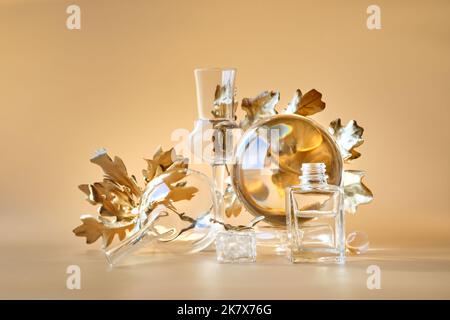 Biophiler Herbsthintergrund. Vergoldete Ahornblätter aus Gold, verzerrt durch transparente Glasgläser, kleine Flaschen. Einfarbig orange beige florale Elemente Stockfoto