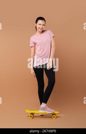 Fröhliche Dame im sportlichen Outfit posiert im Studio mit Skateboard Stockfoto