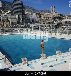 1964, historisch, Blick auf den Staat Nautique Rainier III, ein Schwimmbad mitten in Port Hercule in Monaco, mit einer Haupttauchplattform (nicht im Bild) und kleineren, steinernen Plattformen Poolseite, auf der ein Schwimmer steht. Das Meerwasser-Freibad im olympischen Format wurde im August 1961 offiziell eröffnet. Stockfoto