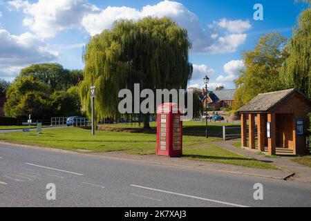 Das Dorfgrün bei Grundisburgh, Suffolk mit der alten Schule im Hintergrund und einer roten Telefondose Stockfoto