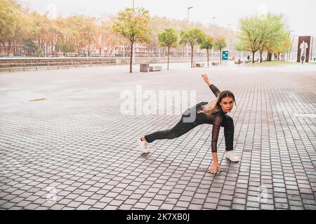 Flexible junge Frau, die im Regen auf der Straße zeitgenössischen Tanz tanzt Stockfoto