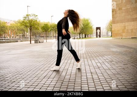 Junge Frau, die im Regen auf der Straße eine Ballettfigur macht Stockfoto