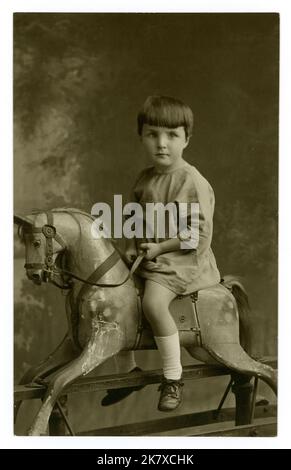 Ursprüngliche Postkarte aus der Zeit der 1920er Jahre mit einem feierlich aussehenden Kind aus den 1920er Jahren auf einem Schaukelpferd, Studio von Charles Winterbourne, Coventry, West Midlands, England, Großbritannien Stockfoto