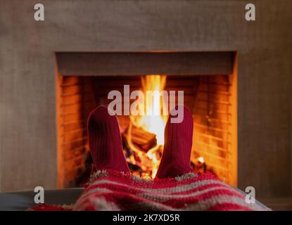 Mann, der sich am brennenden Kamin entspannt. Warme Socken und Decke, Kamin und Flammen, häusliche Innenausstattung. Genießen Sie das Konzept der Einsamkeit. Stockfoto