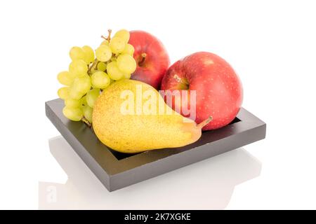 Zwei rote Äpfel, eine grüne Birne und ein Weintraubenzweig auf einem schwarzen Holzteller, Makro, isoliert auf einem weißen Hintergrund. Stockfoto