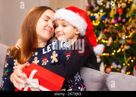 Mutter und Sohn umarmen und schenken zu weihnachten zu Hause im Wohnzimmer Geschenke Stockfoto