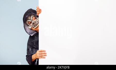 Niedlicher kleiner Junge in einem Kostüm versteckt sich hinter weißem Banner leer Stockfoto