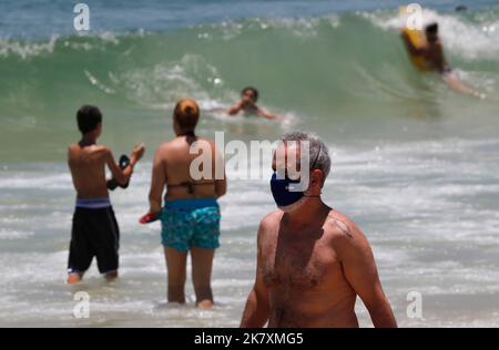 Mann mit Covid-19 Gesichtsmaske am Strand von Cocoaba. Strandgänger sonnen sich am Wochenende in der Nähe der Küste Stockfoto