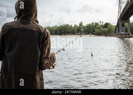 Junger Mann, der am Fluss angeln kann. Fischer hält Spinnrute mit Löffelköder Stockfoto