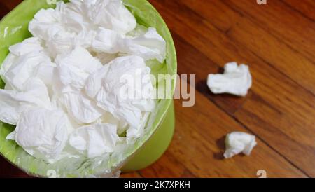 Ein kleiner Papierkorb voll mit gebrauchten Papiertaschentüchern, auf einem Holzboden. Stockfoto