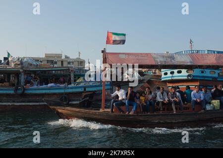 Die Menschen fahren mit einem Abra, einem traditionellen Wassertaxi, das den Dubai Creek von Al Fahidi nach Deira und umgekehrt durchquert. Stadtbild von Old Dubai mit Booten. Stockfoto
