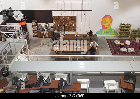 Inside Appetite The Shop, ein Bio-Café in Dubai, VAE. Der Industrieinnenraum hat Gäste in langen Bänken und Tischen. Wandpfosten-seine Form Van Gogh Gesicht. Stockfoto