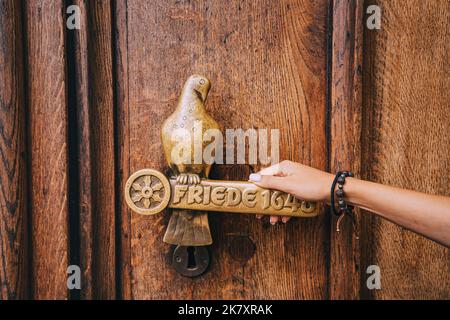 25. Juli 2022, Osnabruck, Deutschland: Weibliche Touristenhand öffnet Eisernen alten Griff mit Taube einer Holztür eines historischen Rathauses. Stockfoto