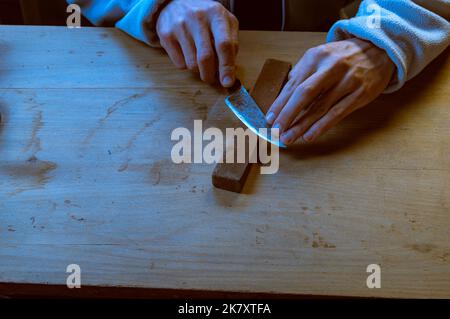 Ein Mann hält ein Messer in der Hand. Ein Mann schärft ein Messer auf einem Schleifstein. Manuelles Schärfen des Messers. Blick von oben. Stockfoto