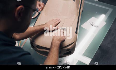 Zwei männliche Automobildesigner modellieren futuristisches Knetmasse-Modell eines Autos mit Rechen. Zukünftiges Design von Elektroautos der neuen Generation. Arbeiten im modernen Auto-Design-Studio. Stockfoto