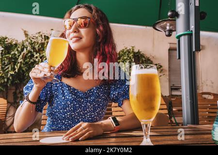 Ein Mädchen in Pub oder Bar trinkt kühles und erfrischendes, leicht gefiltertes Bier aus Gläsern. Feier und alkoholische Getränke Konzept Stockfoto