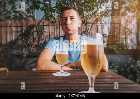 Ein lustiger betrunkener Mann trinkt in einer Bar, einem Pub oder einem deutschen Biergarten frisch gebrautes leichtes Bier aus Gläsern Stockfoto