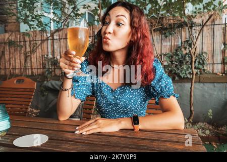 Lustiges betrunkenes Mädchen, das in einer Bar, einem Pub oder einem deutschen Biergarten frisch gebrautes leichtes Bier aus Gläsern verkostet Stockfoto