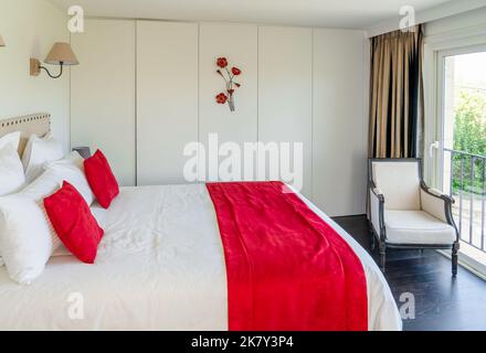 Stilvolles, modernes französisches Schlafzimmer mit einem Kingsize-Bett in Rot und Weiß Stockfoto