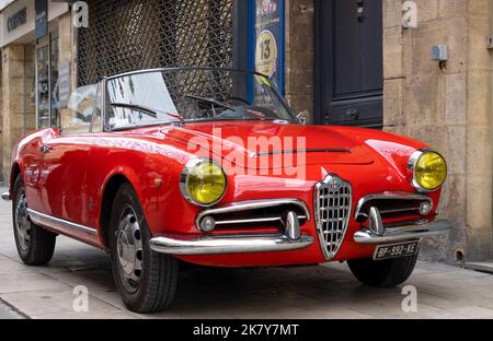 Ein klassischer Alfa Romeo 'Rosso Corsa' Spider Giula wartet auf den Eintritt zur Oldtimer- und Fahrradshow im Stadtzentrum von Sarlat-la-Caneda Stockfoto