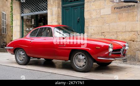 Ein klassischer Alfa Romeo 'Rosso Corsa' Giula SS Berlinetta Sprint Speciale wartet auf den Eintritt zur Oldtimer- und Fahrradmesse im Stadtzentrum von Sarlat-la-Caneda Stockfoto