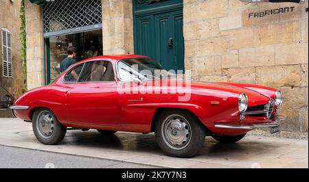 Ein klassischer Alfa Romeo 'Rosso Corsa' Giula SS Berlinetta Sprint Speciale wartet auf den Eintritt zur Oldtimer- und Fahrradmesse im Stadtzentrum von Sarlat-la-Caneda Stockfoto