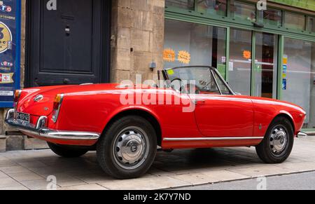 Ein klassischer Alfa Romeo 'Rosso Corsa' Spider Giula wartet auf den Eintritt zur Oldtimer- und Fahrradshow im Stadtzentrum von Sarlat-la-Caneda Stockfoto