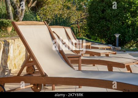 Eine Reihe leerer Sonnenliegen zum Sonnenbaden aus Holz am Pool bei der Morgensonne Stockfoto