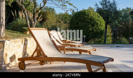 Eine Reihe leerer Sonnenliegen zum Sonnenbaden aus Holz am Pool bei der Morgensonne Stockfoto