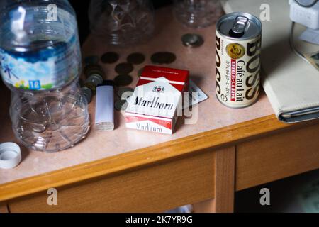 Unordentlicher kleiner Holzschreibtisch im Hotelzimmer mit Wasserplastikflaschen und japanischen Banknoten und Münzen und Zigarettenpackung, Kaffee in Dosen und Ladegerät. Stockfoto