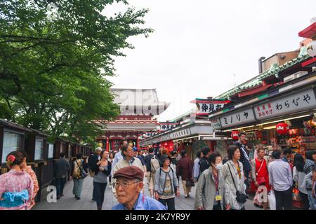 Blick auf die Einkaufsstraße Nakamise im Sensoji-Tempelkomplex mit Menschenmassen, die Souvenirs einkaufen, spazieren gehen und Wolken im hellen Himmelshintergrund. Stockfoto