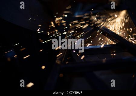 Schleifen von Stahl. Funken aus Metall. Heiße Partikel. Kleine Lampen. Arbeiten am Metallprofil. Stockfoto