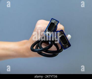 Schwarzes VGA-Kabel mit Handhaltung. Die Hand des Mannes hält einen VGA-Anschluss. Closeup VGA-Kabel.Selektiver Fokus und geringe Schärfentiefe. Stockfoto