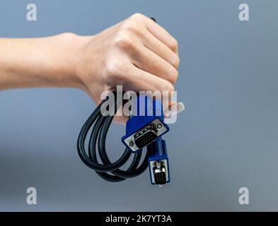 Schwarzes VGA-Kabel mit Handhaltung. Die Hand des Mannes hält einen VGA-Anschluss. Closeup VGA-Kabel.Selektiver Fokus und geringe Schärfentiefe. Stockfoto