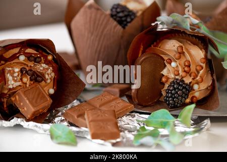 Schokoladen-Cupcake mit Brombeeren und Eukalyptusblättern auf Silberfolie. Schokoladendessert. Süßigkeiten und Desserts. Backwaren Stockfoto