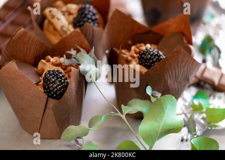 Schokoladendessert. Schokoladen-Cupcake mit Brombeeren- und Eukalyptusblättern auf Silberfolie. Verschiedene süße Tische. Süßigkeiten und Desserts. Backwaren Stockfoto