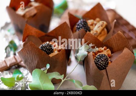 Schokoladen-Cupcake mit Brombeeren und Eukalyptusblättern auf Silberfolie. Schokoladendessert. Süßigkeiten und Desserts. Stockfoto